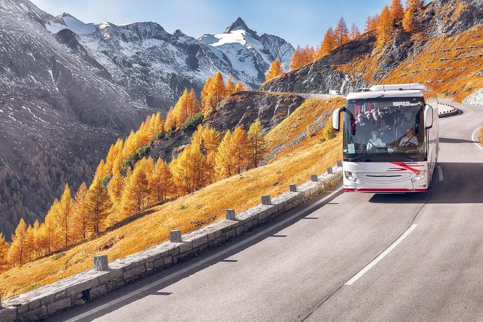Autocar turístico recorriendo una carretera panorámica entre montañas y paisajes alpinos.